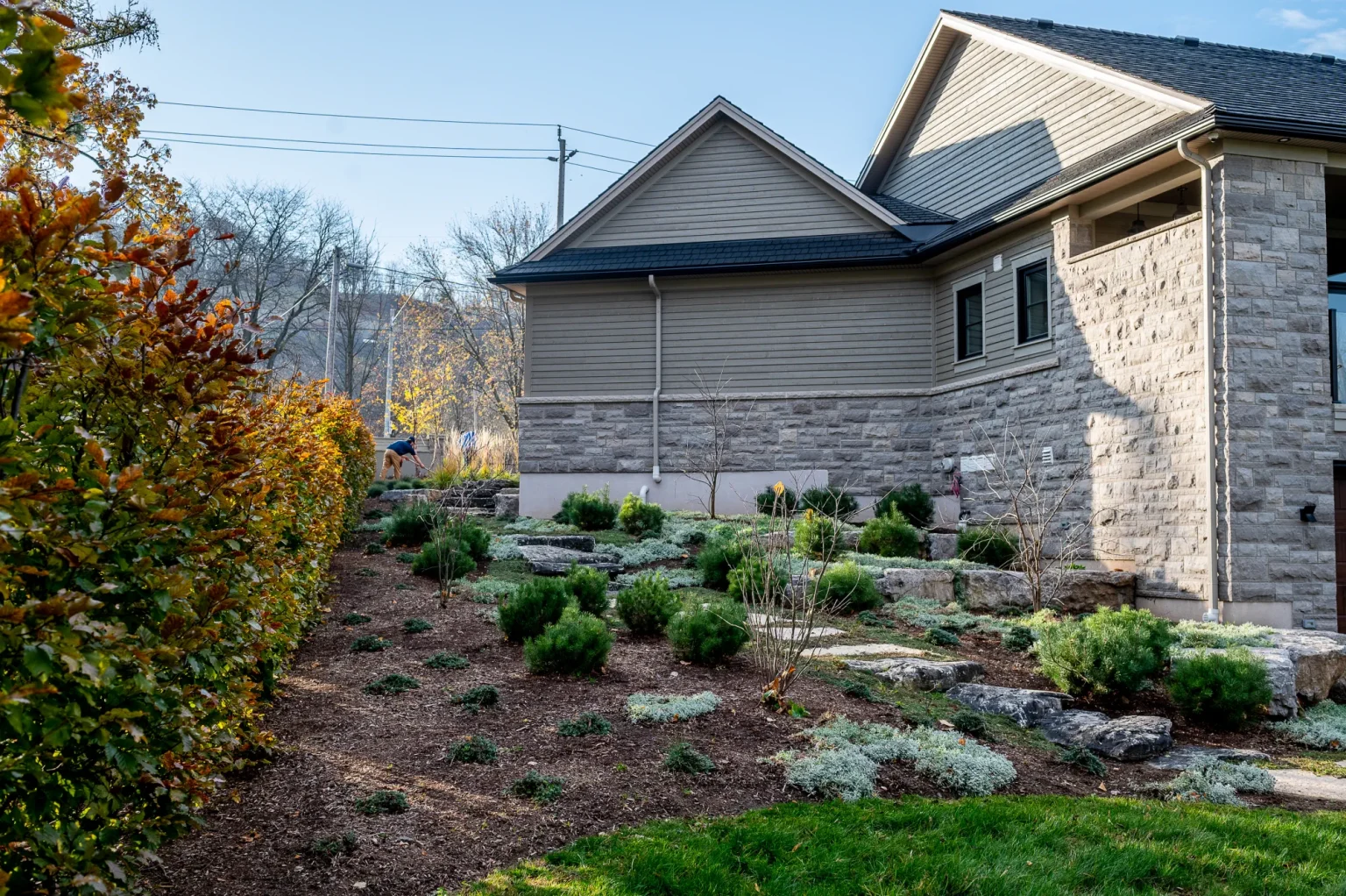 Wide autumn view of a landscaped side garden with stone features and mulched planting beds in Ancaster.