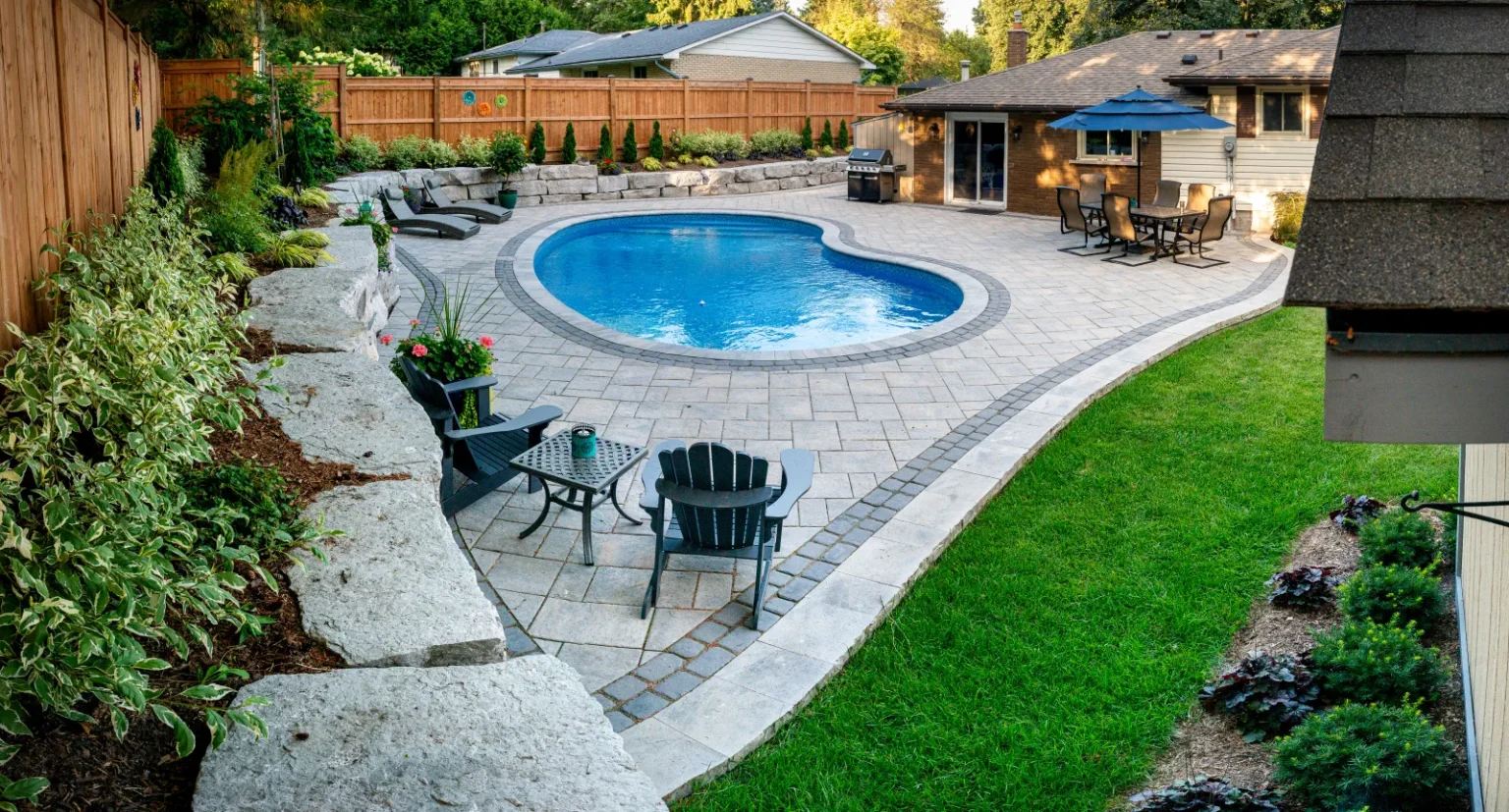 Wide elevated corner view of the pool, interlock patio, lawn and armour stone retaining in Ancaster.
