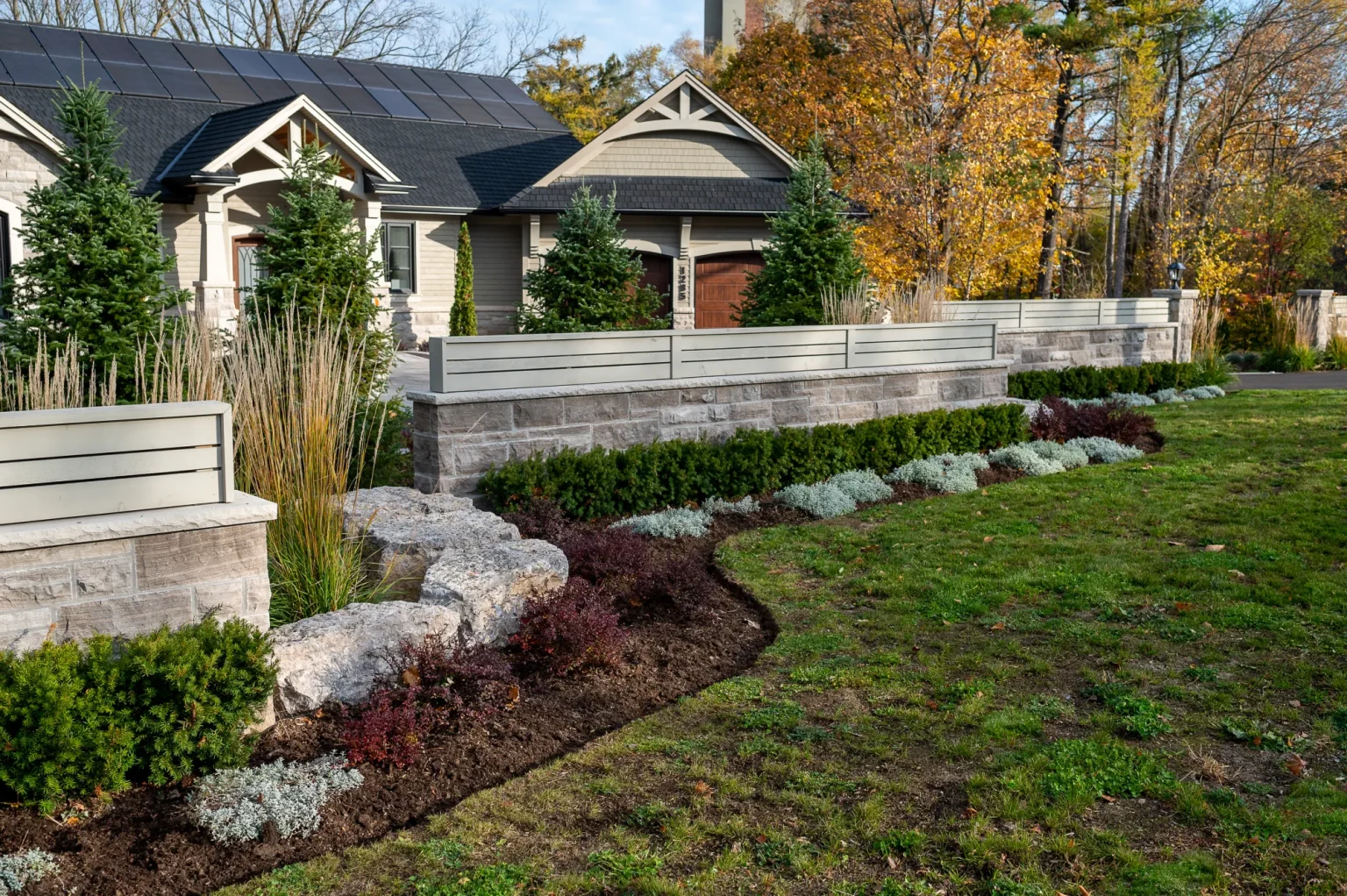 Broad landscaped yard with decorative screening, boulders and layered planting in Ancaster.