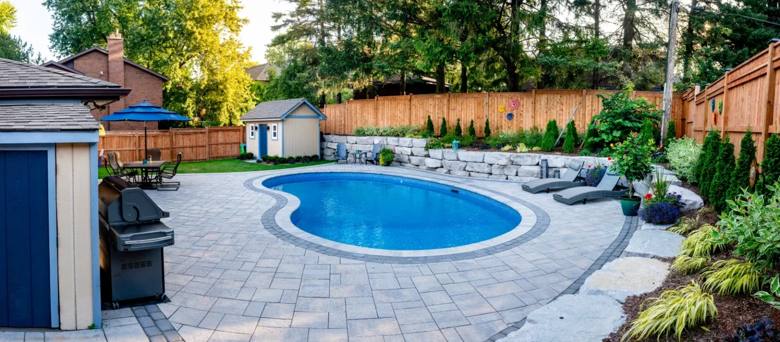 Wide pool-deck view with interlock paving, armour stone retaining and privacy fencing in Ancaster.