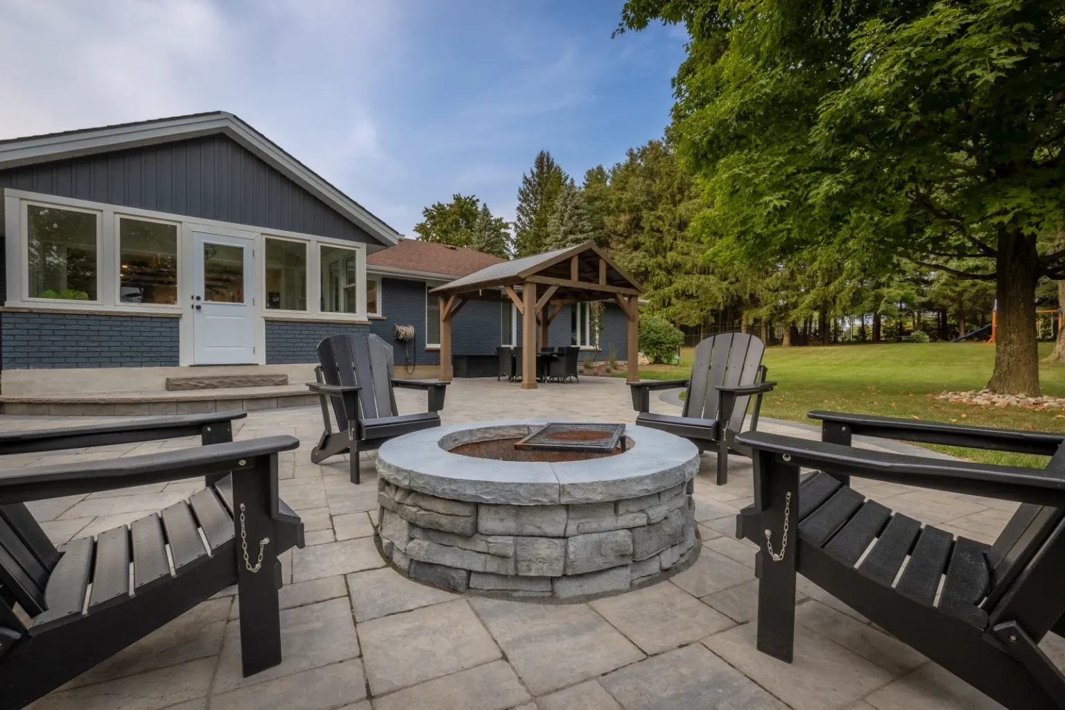 Circular stone fire pit with Adirondack chairs on an interlock patio in Brantford.