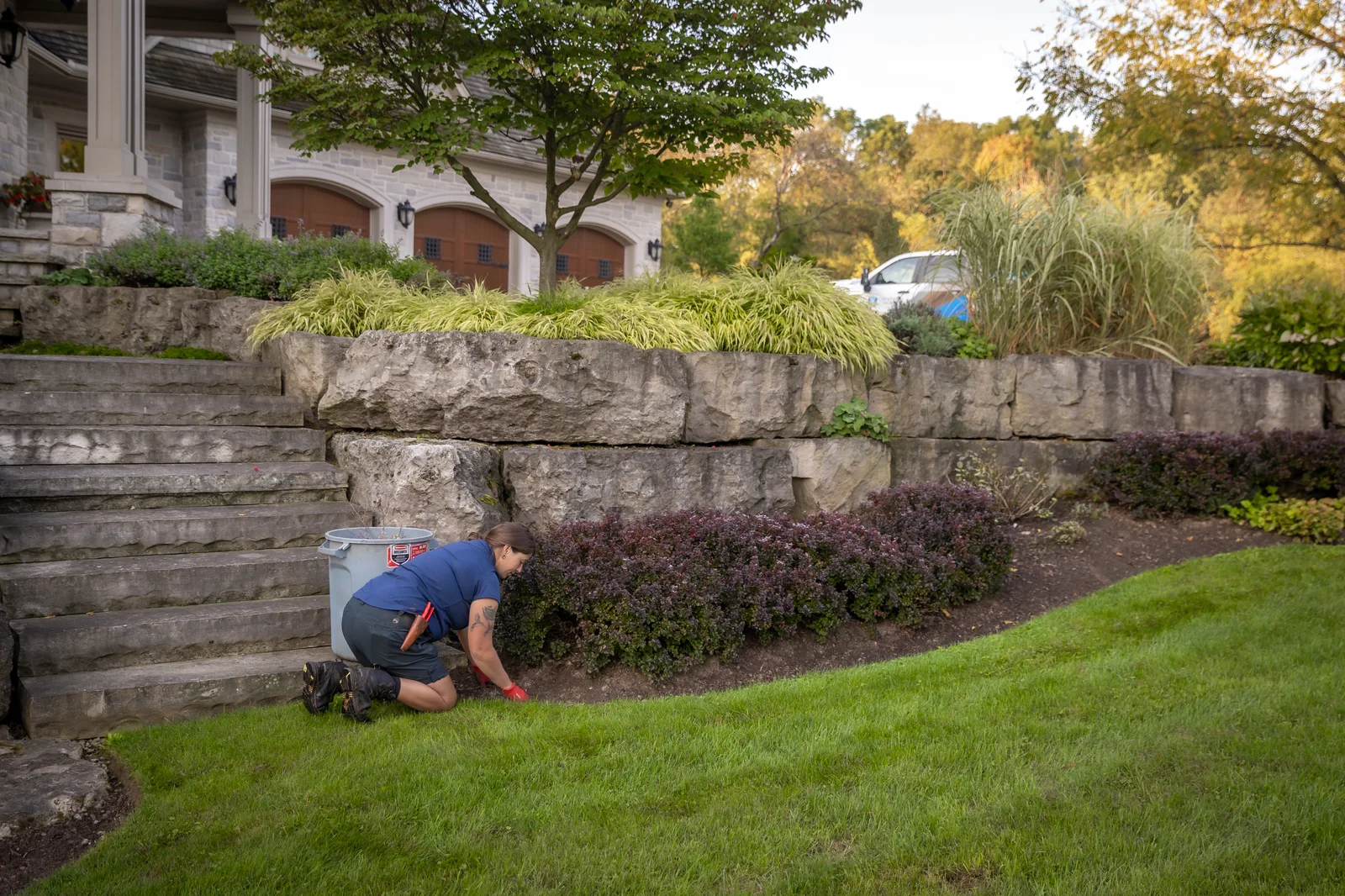 Creative Concepts crew member tending a residential garden bed below a stone retaining wall.