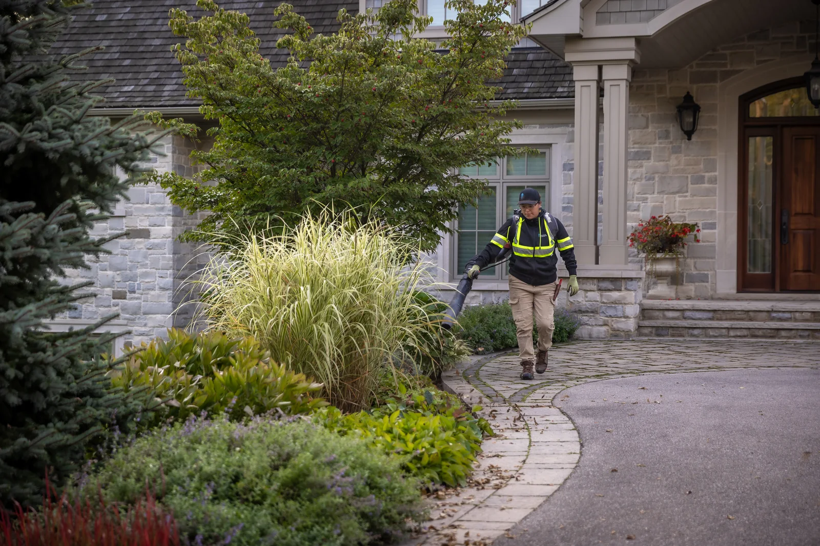 Creative Concepts crew member using a leaf blower along a landscaped residential front entry.