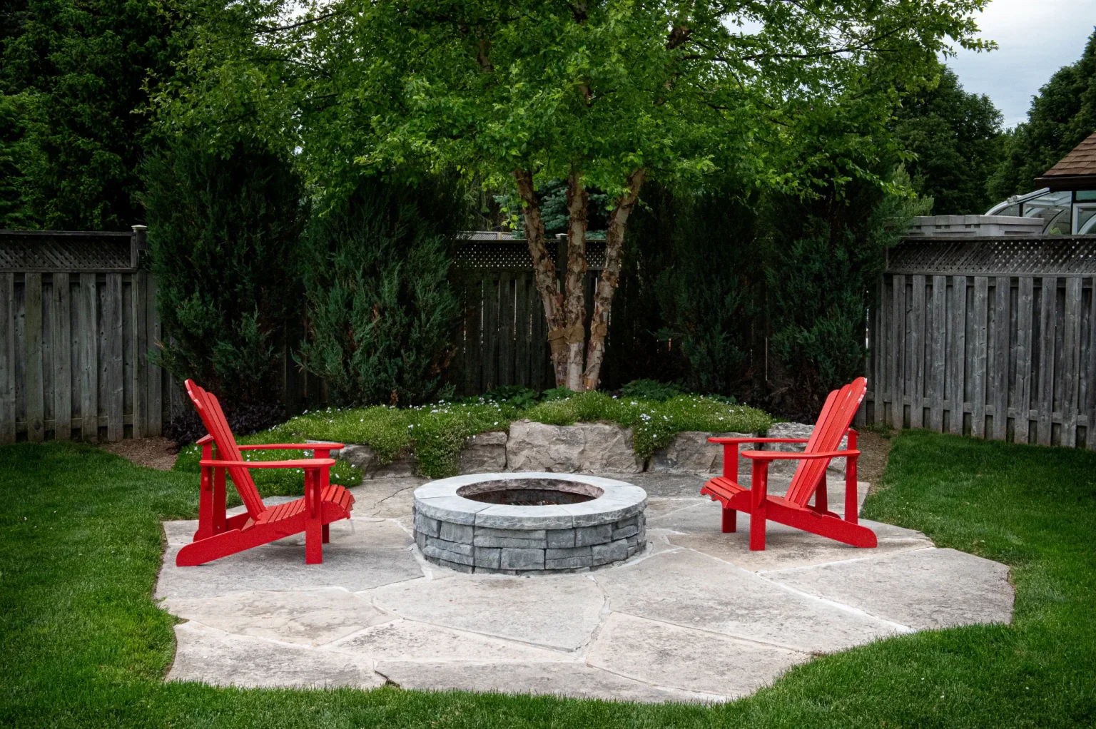Backyard fire pit area with red Adirondack chairs and stone paving in Dundas.