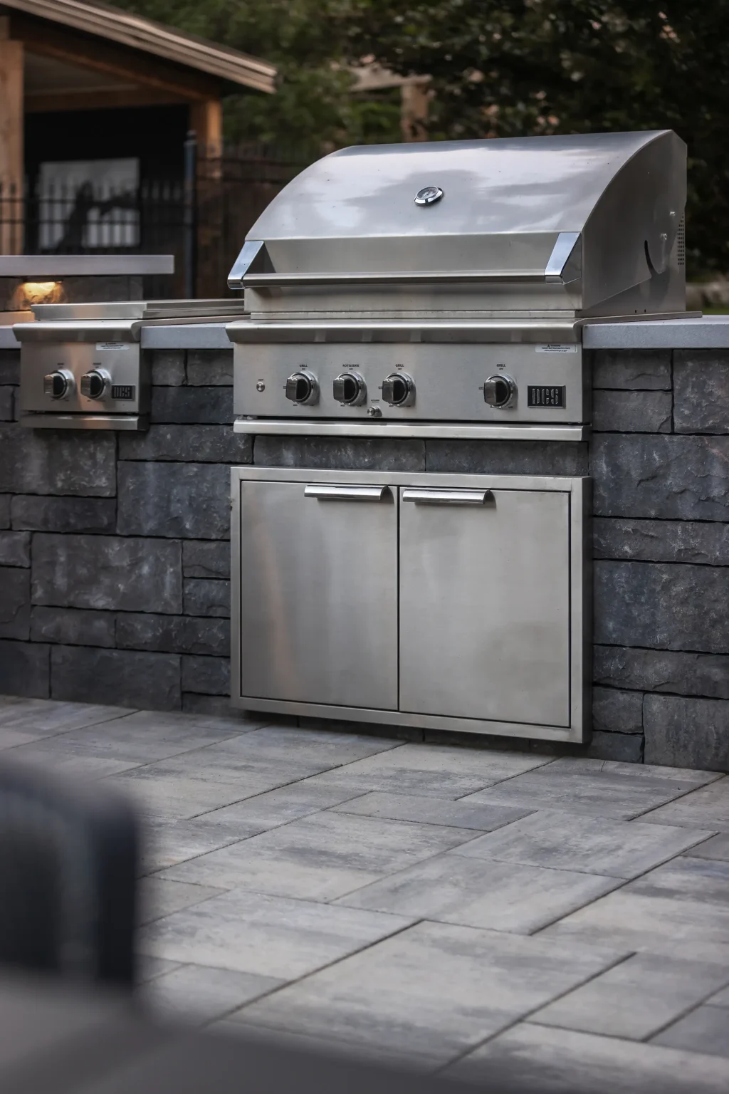 Built-in stainless barbecue integrated into a dark masonry outdoor kitchen in Dundas.