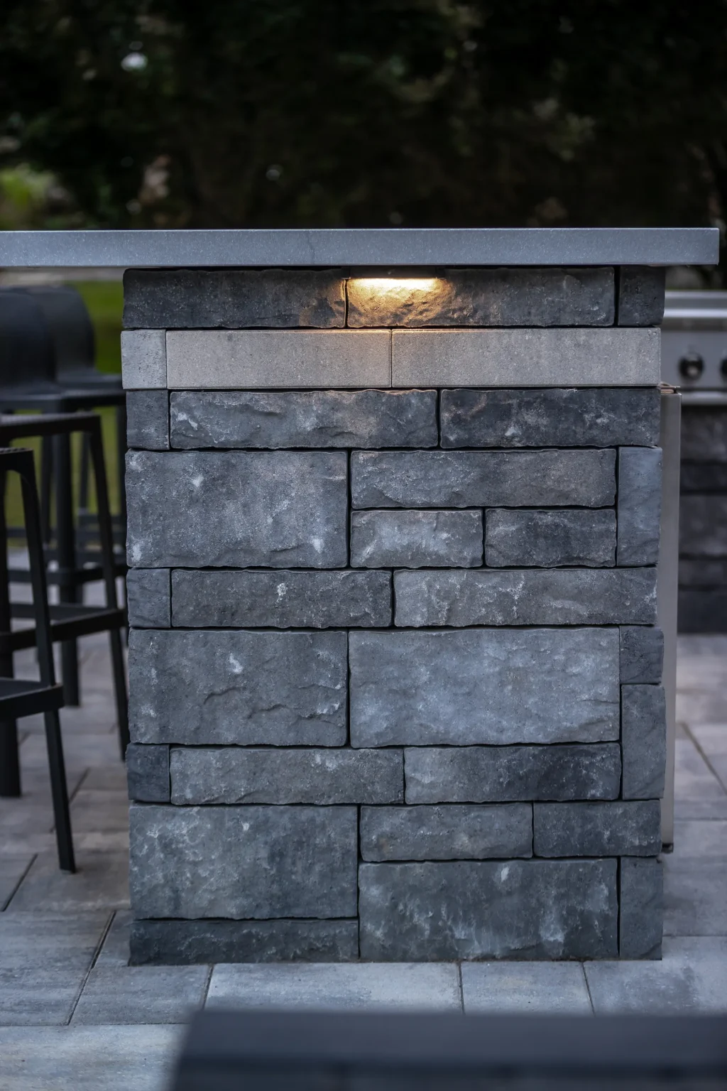 Dark masonry outdoor-kitchen wall with integrated lighting beside the patio in Dundas.
