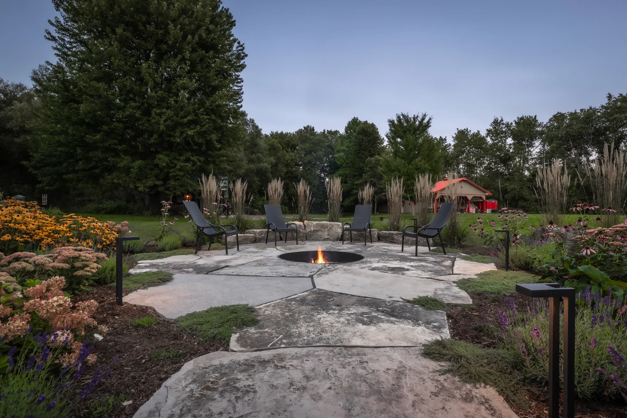 A natural-stone fire-pit patio surrounded by flowering perennials, ornamental grasses and mature trees in Dundas.