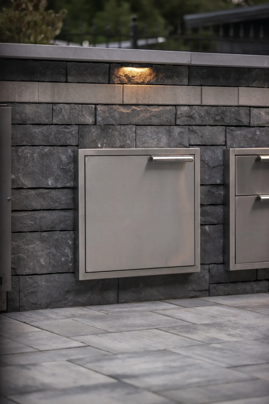 Close detail of a stainless access door set into a dark masonry outdoor-kitchen wall in Dundas.