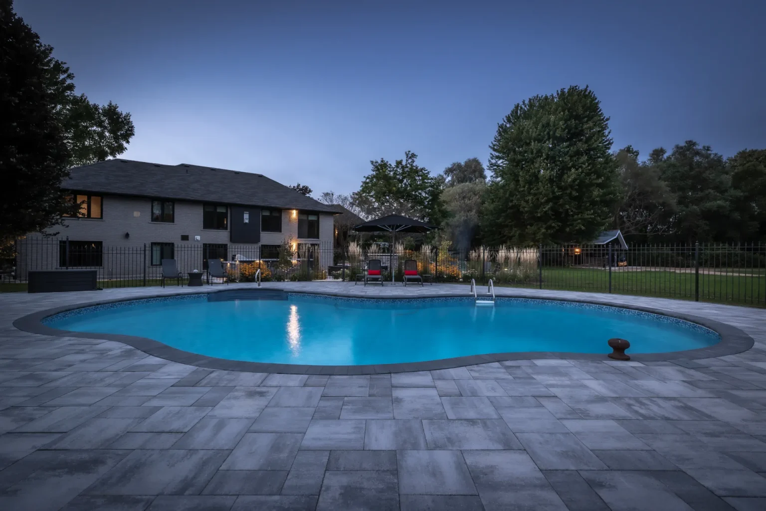 Wide dusk view across the curved pool and surrounding patio in Dundas.