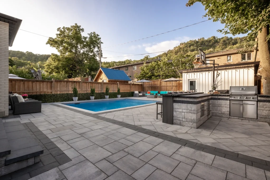 Wide establishing view of the rectangular pool, paver patio, outdoor kitchen and seating in Dundas.
