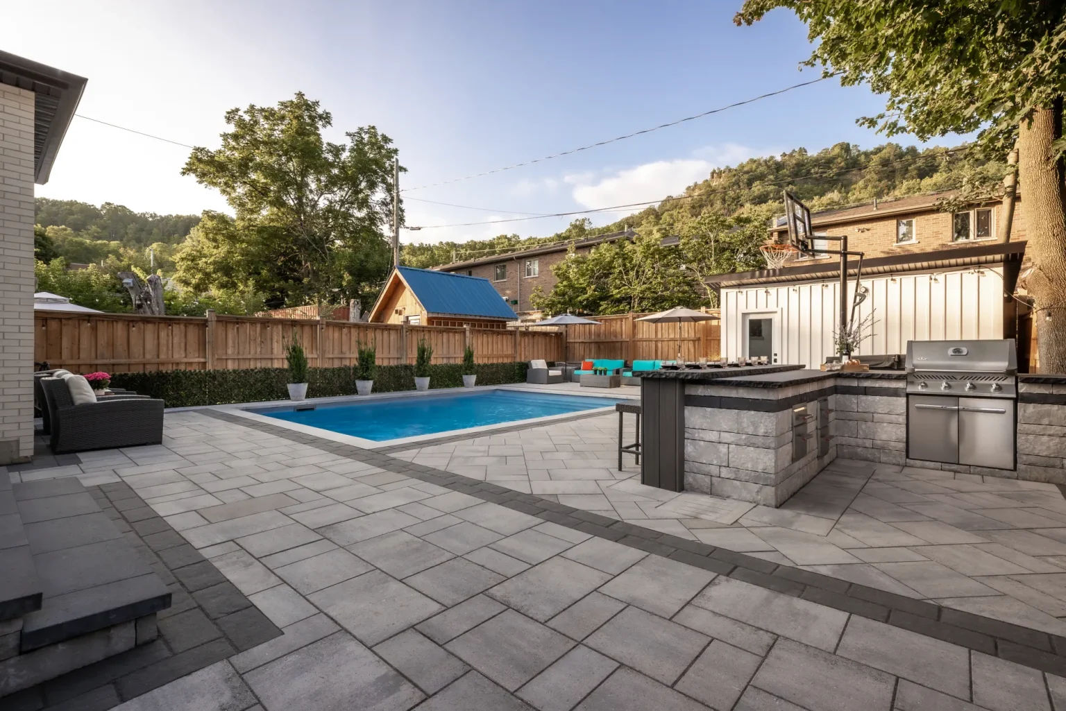 Wide establishing view of the rectangular pool, paver patio, outdoor kitchen and seating in Dundas.
