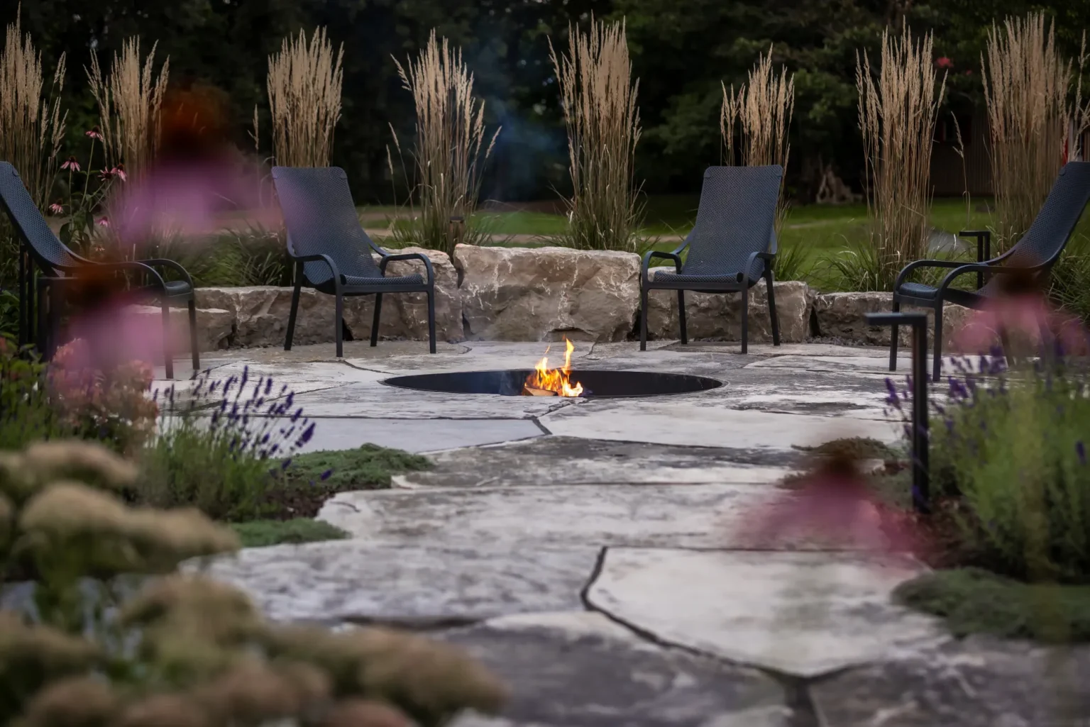 Fire-pit garden viewed through flowering plants and natural stone paving in Dundas.