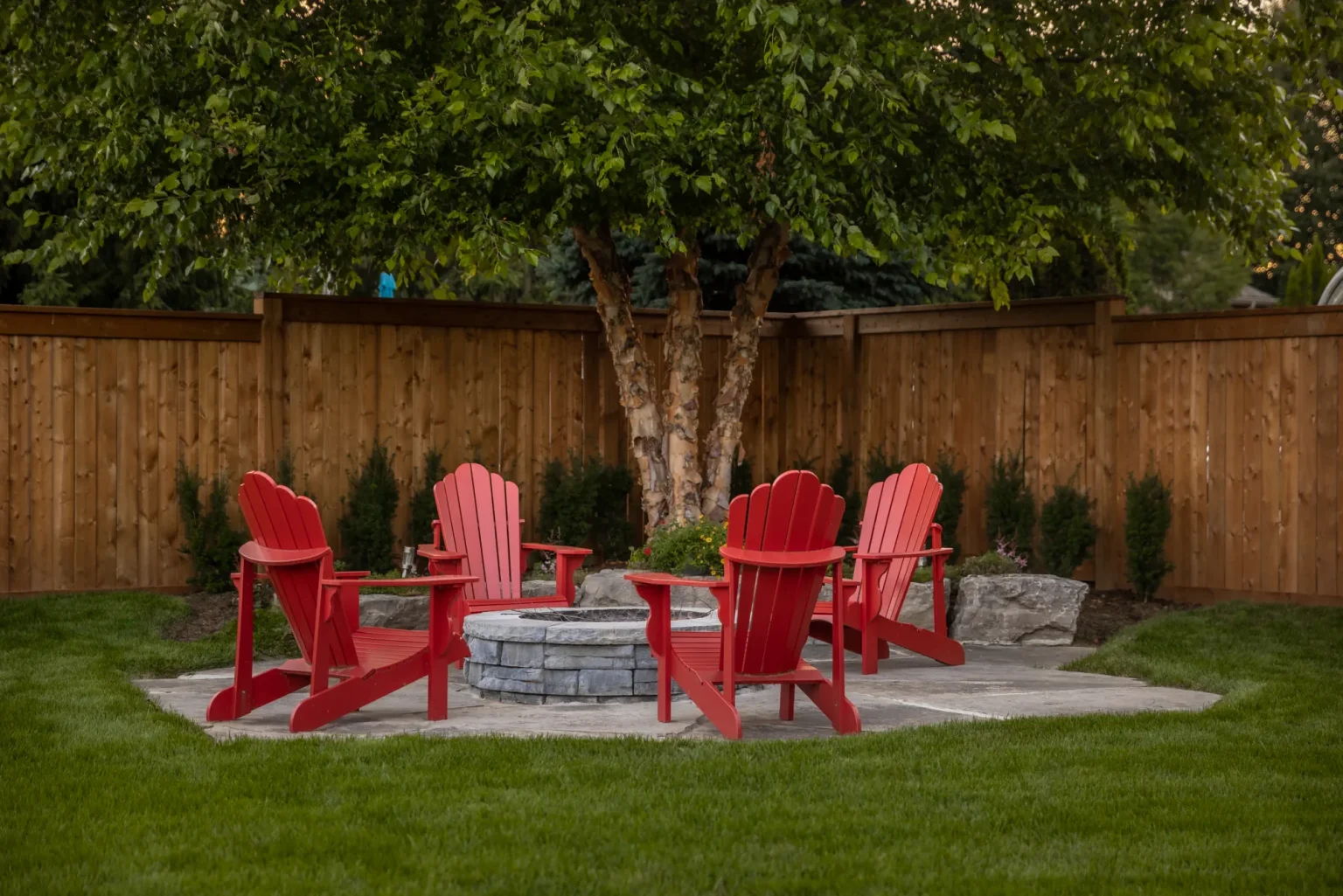 Stone fire pit and red Adirondack seating area in a Dundas backyard.
