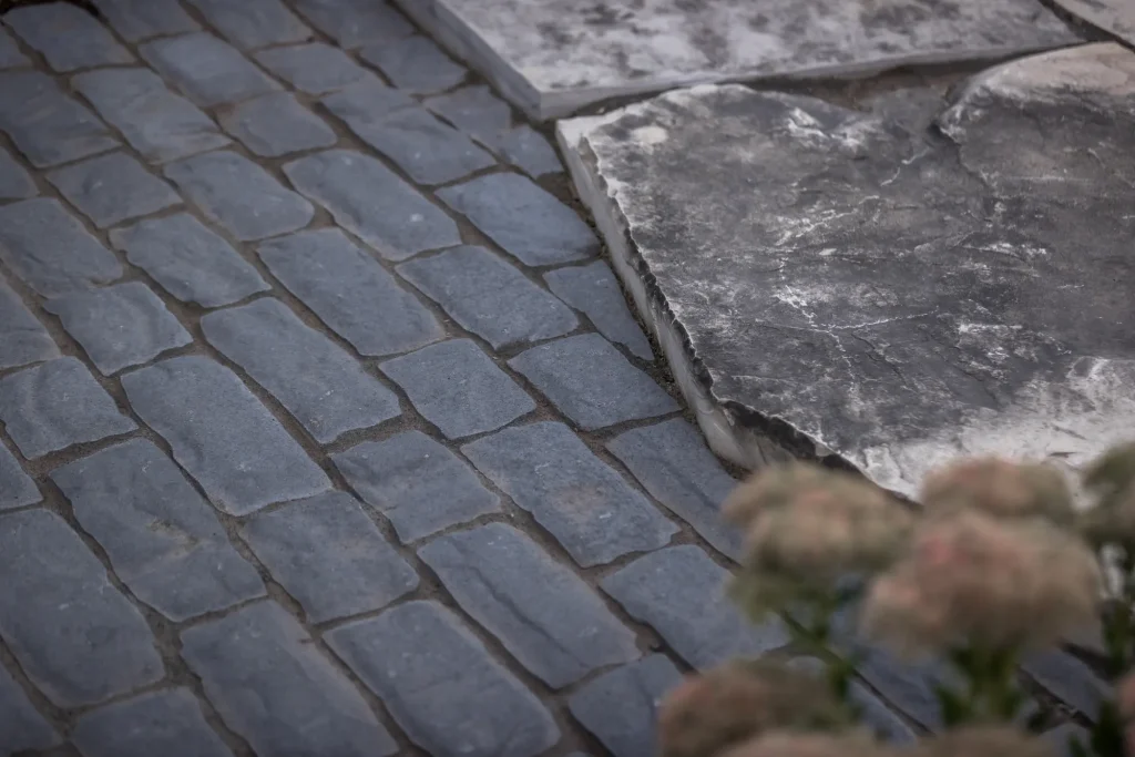 Close hardscape detail where natural stone slabs meet dark paver edging.