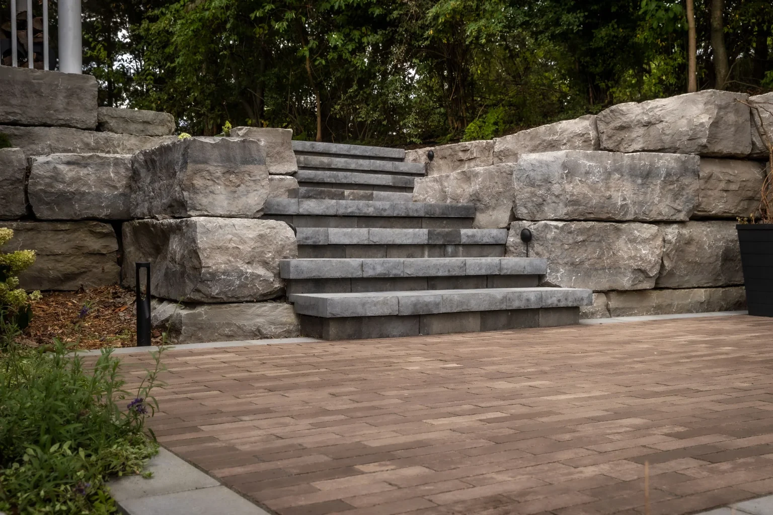 Wide view of central cascading grey stone stairs flanked by oversized rough-cut armour-stone retaining blocks and a paved terrace in Dundas.