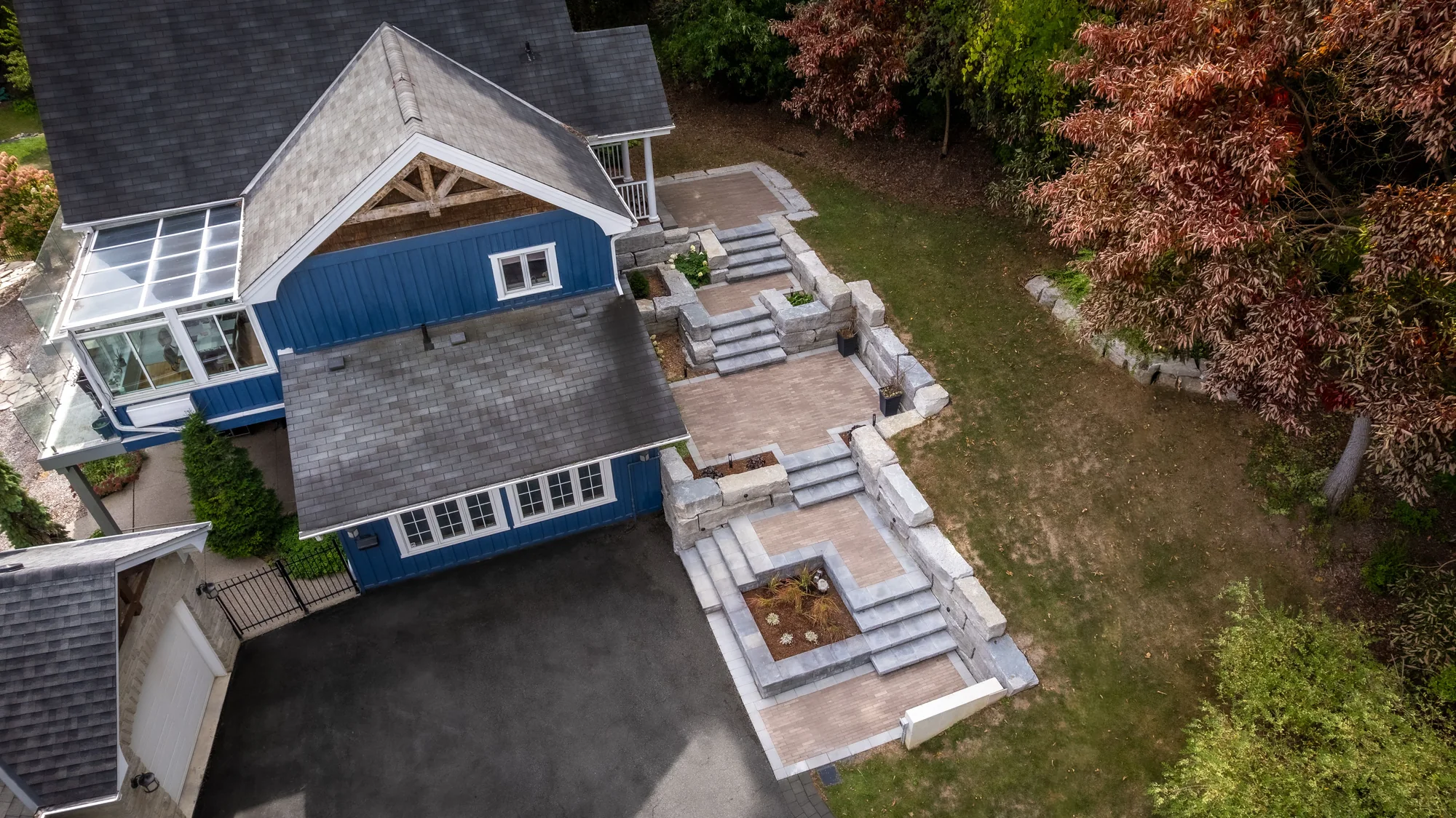 Stone stairs and terraced retaining walls with planted beds beside a blue home in Dundas, viewed from above.