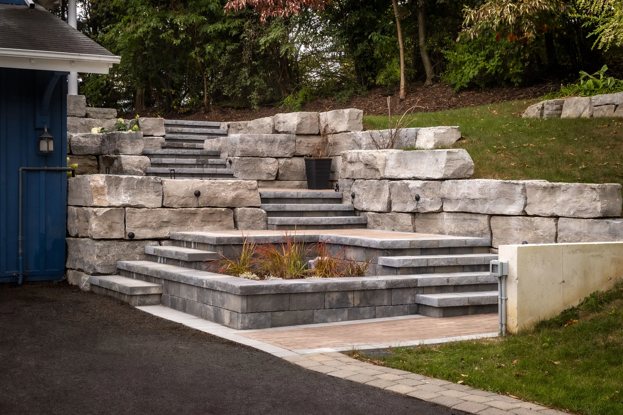 Natural-stone steps and terraced retaining walls beside a blue home and planted entrance in Dundas.