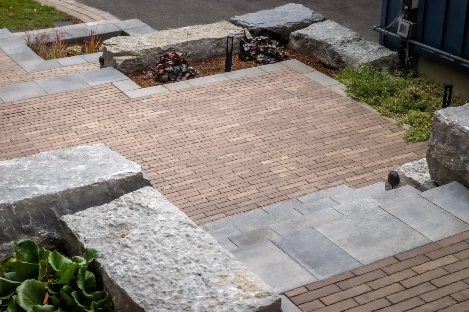 High oblique view of a paved terrace bordered by massive limestone-coloured stone retaining blocks and steps, with small planting pockets in Dundas.