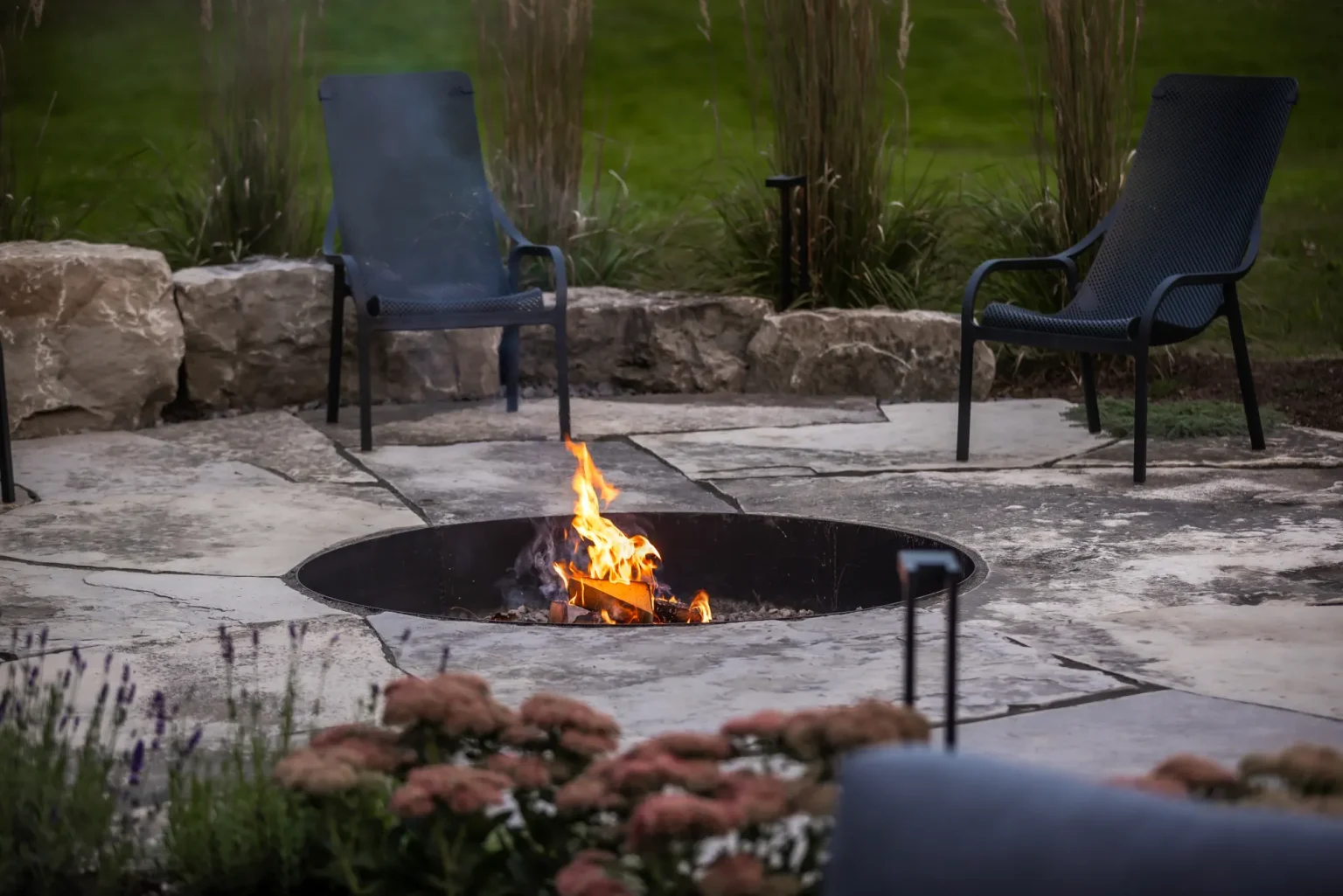 Natural-stone fire-pit patio with lounge chairs surrounded by garden planting in Dundas.
