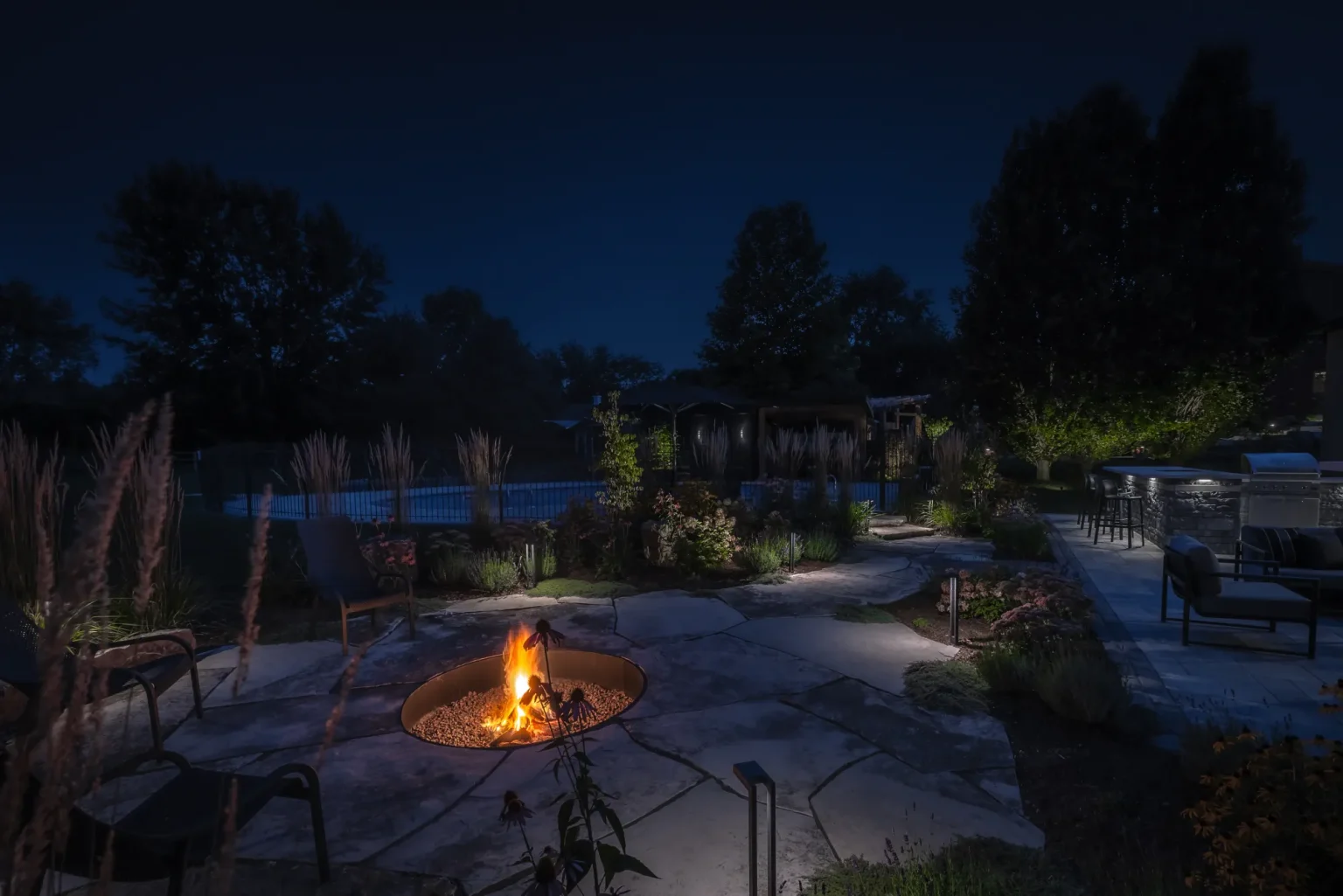 Wide night view combining the fire-pit garden, pool area and landscape lighting in Dundas.