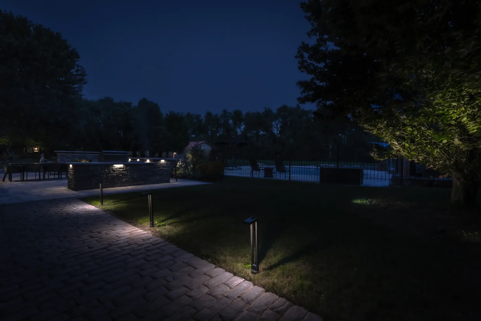 Night view of the illuminated path and lawn leading toward the outdoor kitchen in Dundas.