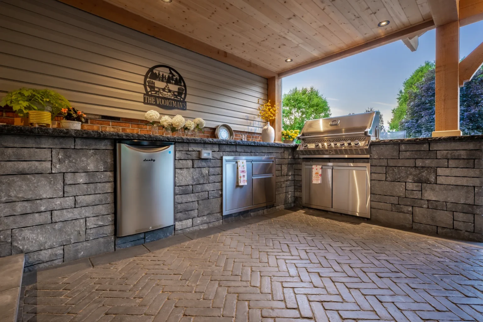 Grill, refrigerator and stone-clad cabinetry in the covered Dundas outdoor kitchen.