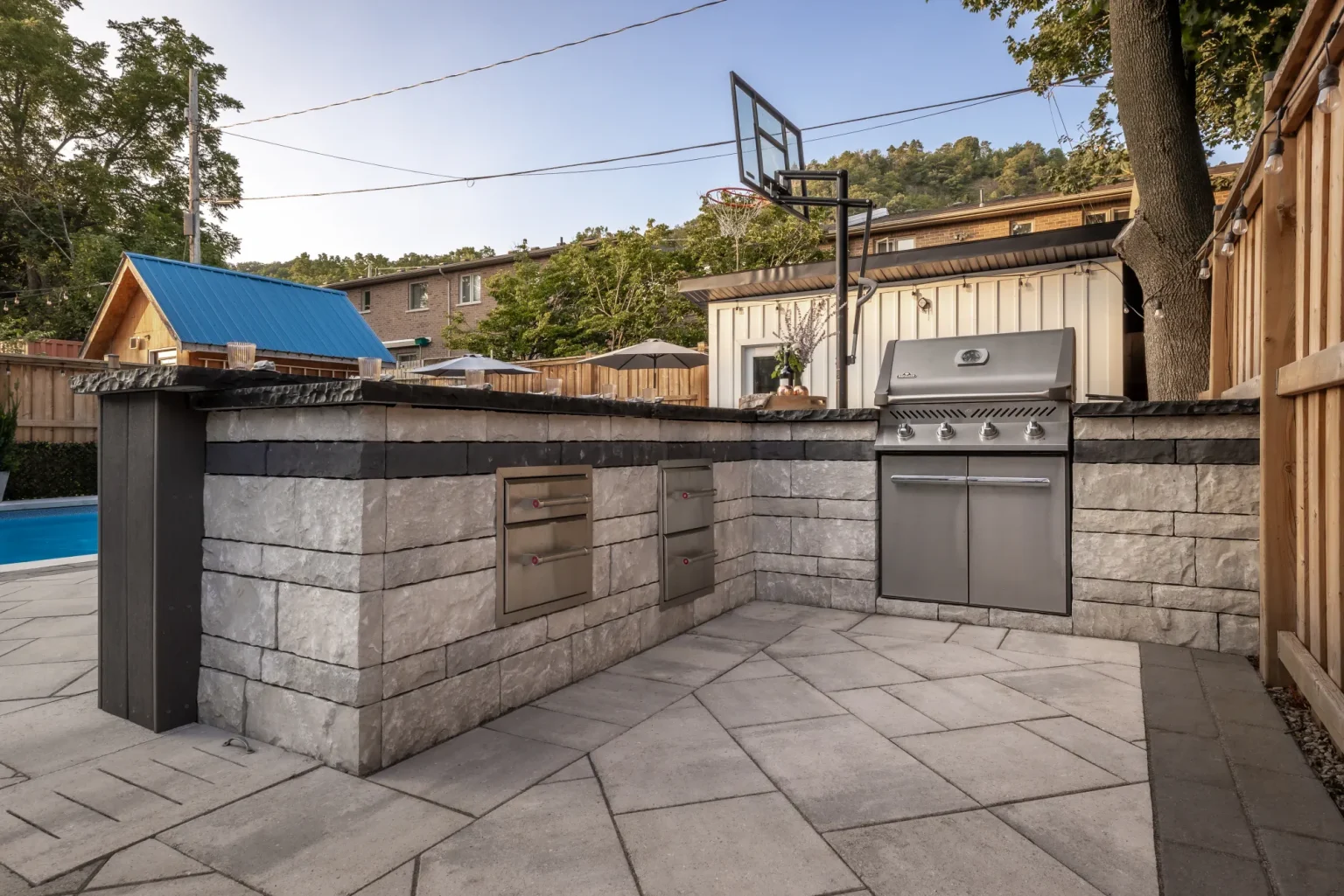 Outdoor kitchen and barbecue built into masonry walls beside the pool patio in Dundas.