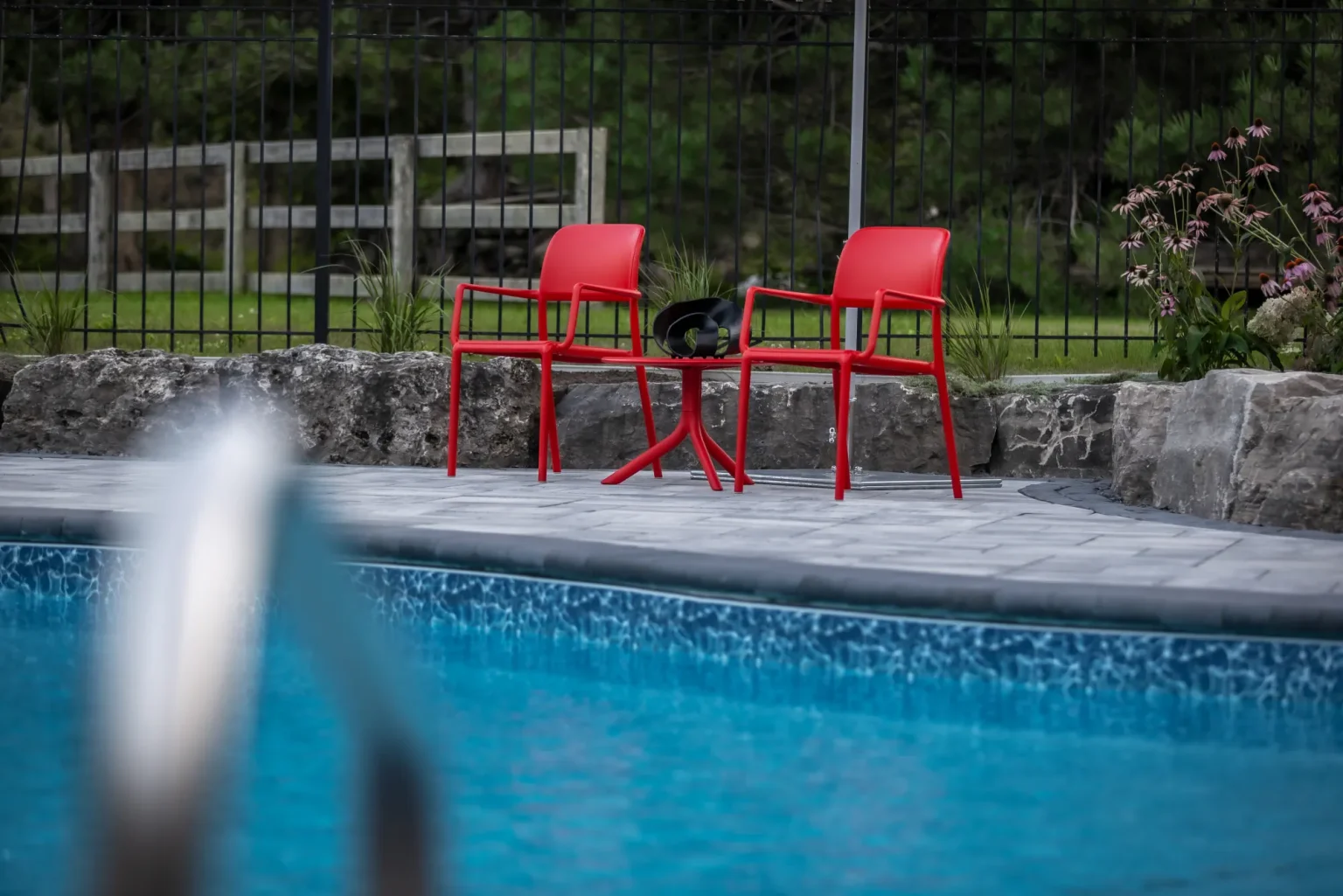 Pool view toward bright red chairs and the natural-stone garden beyond in Dundas.