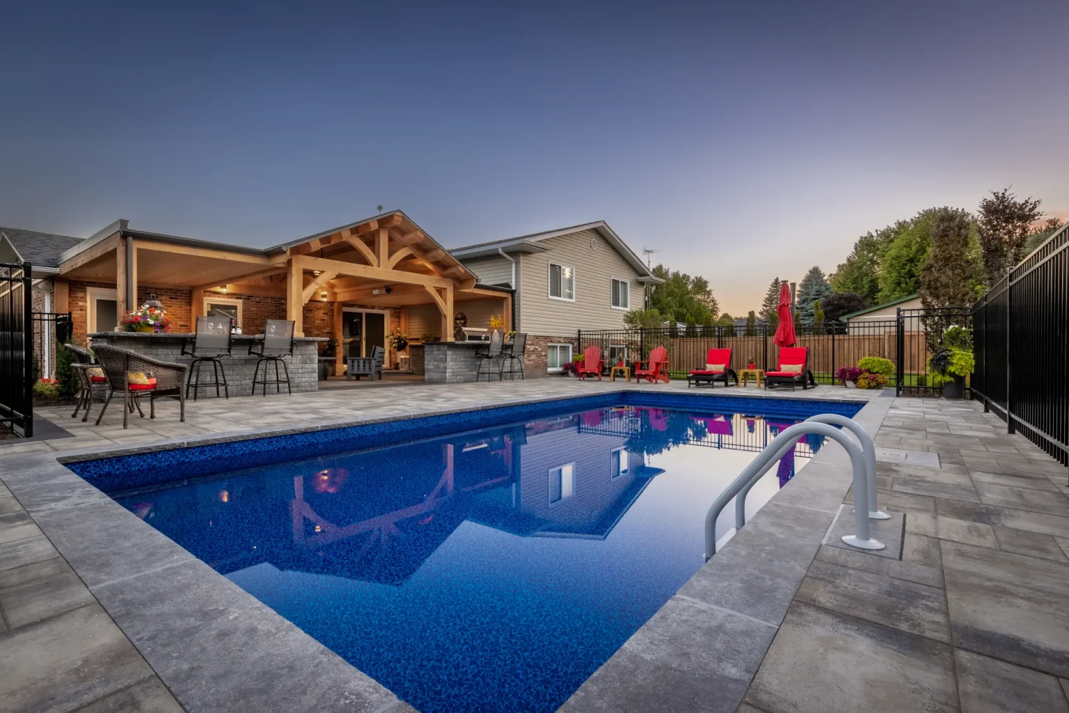 Pool, stone patio and house-connected timber frame at dusk in Dundas.