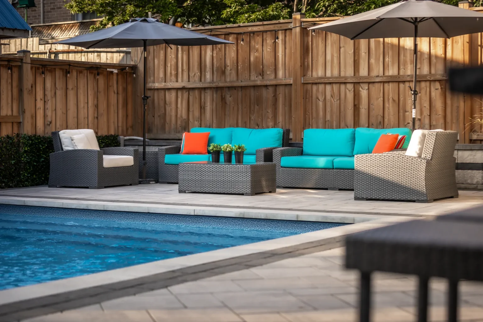 Poolside lounge seating with colourful cushions against a privacy fence in Dundas.