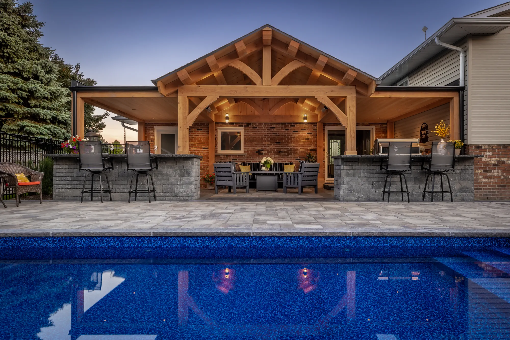 Timber pavilion and outdoor bar viewed across a Dundas backyard pool.