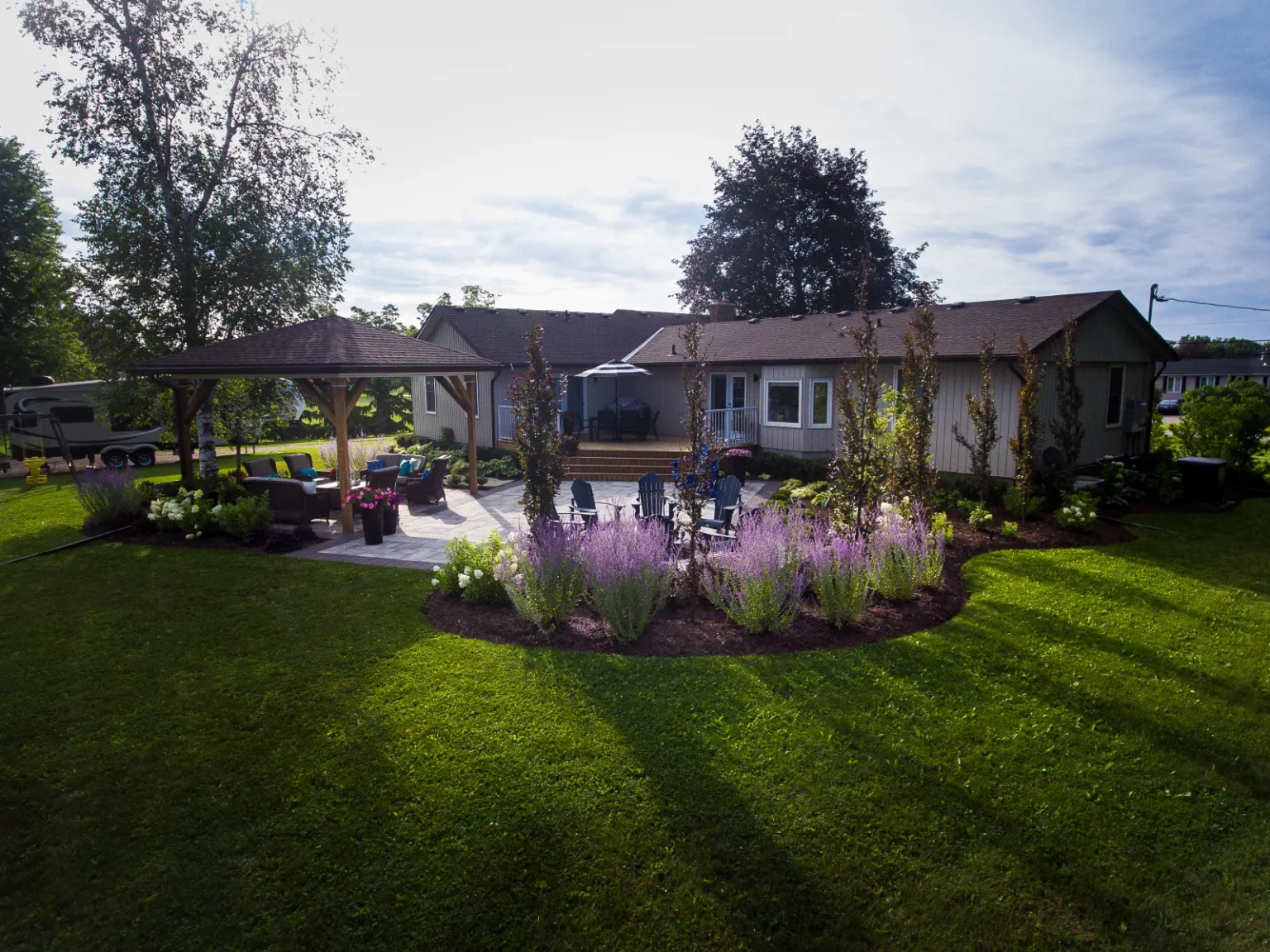 Ground-level wide view of the backyard gathering spaces framed by lawn and planting in Flamborough.