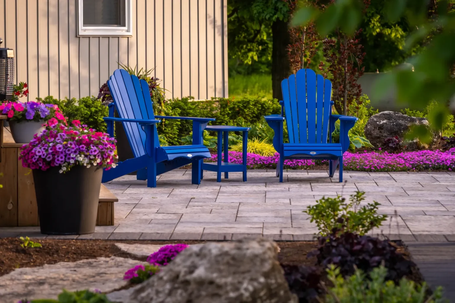 Blue Adirondack chairs on the paver patio framed by flowers and stone accents in Flamborough.