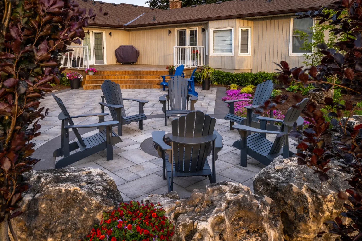 Circular fire-pit patio with Adirondack seating framed by boulders and flowers in Flamborough.