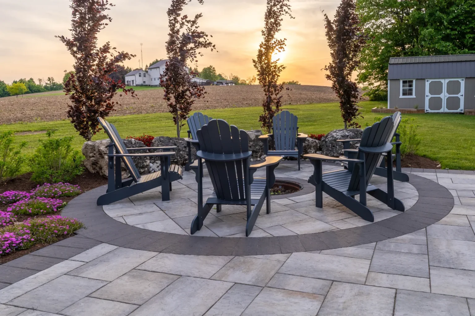 Fire-pit seating circle at sunset with contrasting paver border and flowering groundcover in Flamborough.