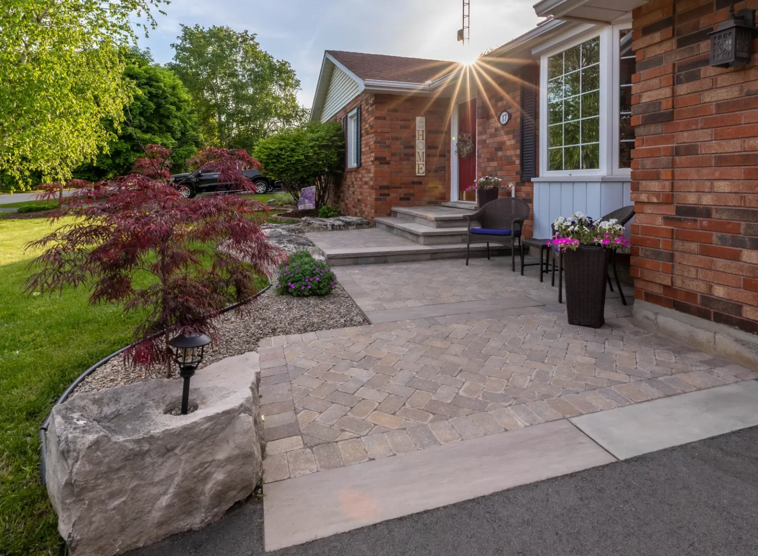 Wide front entry patio and walkway with stone accents, a Japanese maple and layered planting in Flamborough.