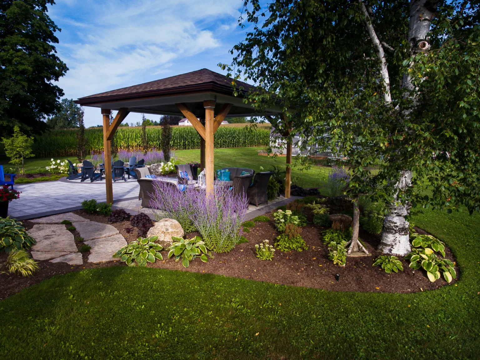 Garden-level view of the timber pavilion framed by boulders, flowering perennials and lawn in Flamborough.
