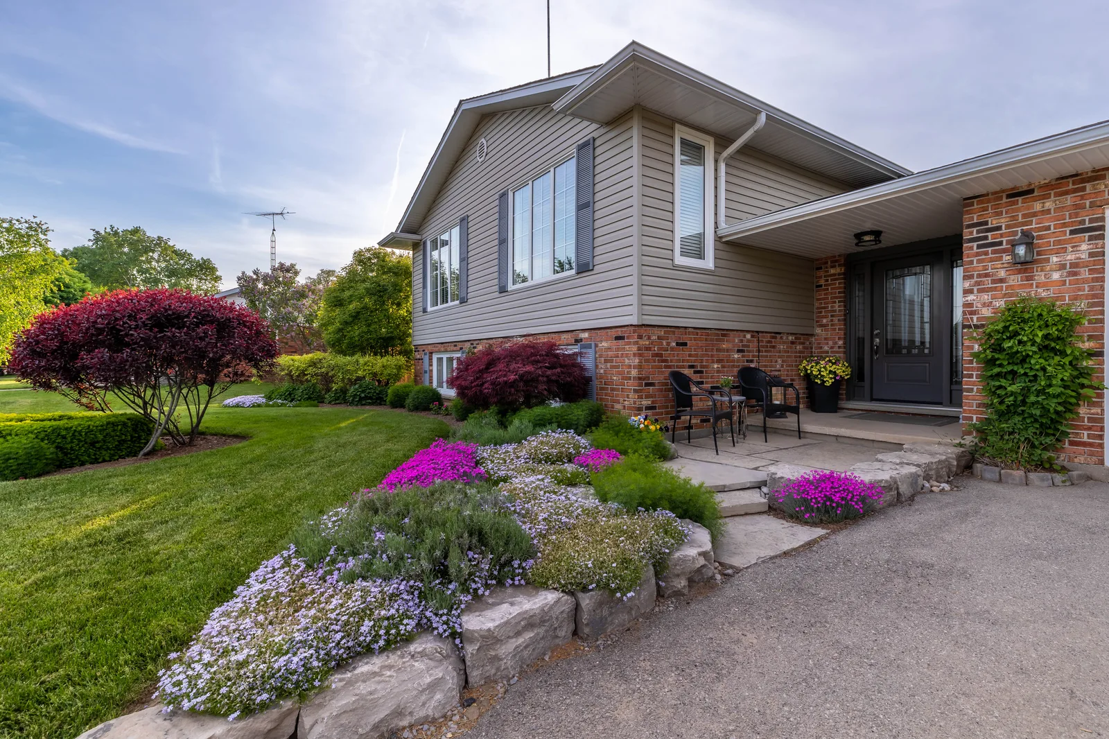 A residential entrance framed by Japanese maples, flowering groundcover and a natural stone garden border.