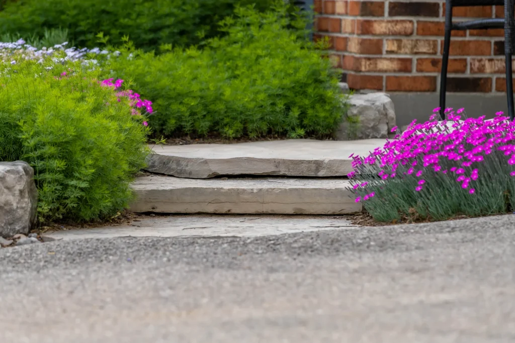 Natural stone steps framed by green planting and magenta flowers beside a brick home.