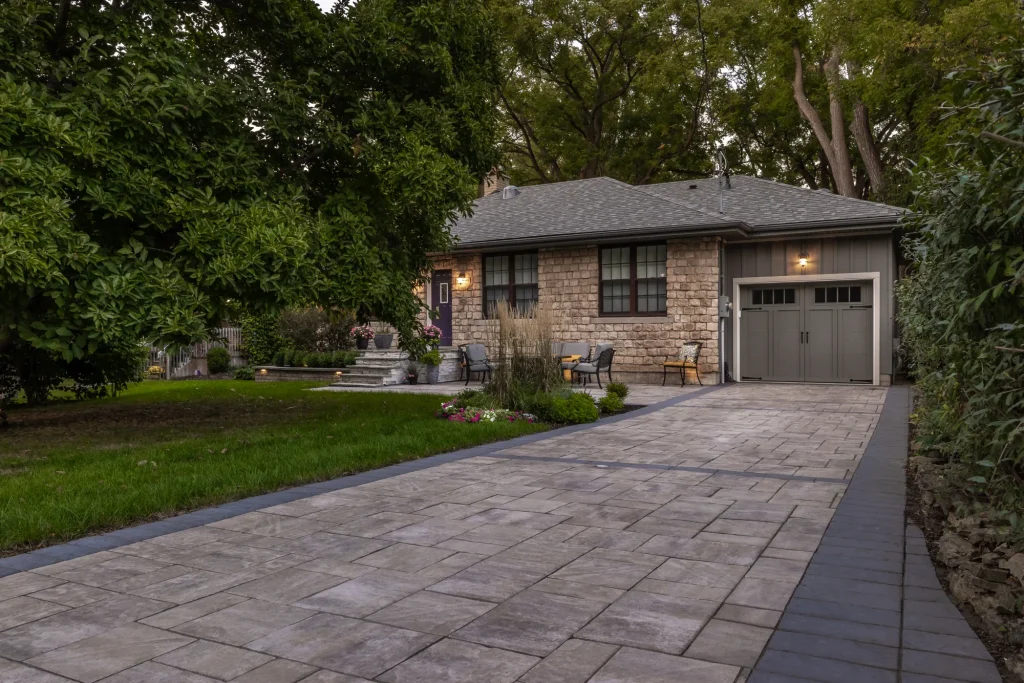 Wide driveway and garage view with pavers, border and lawn.