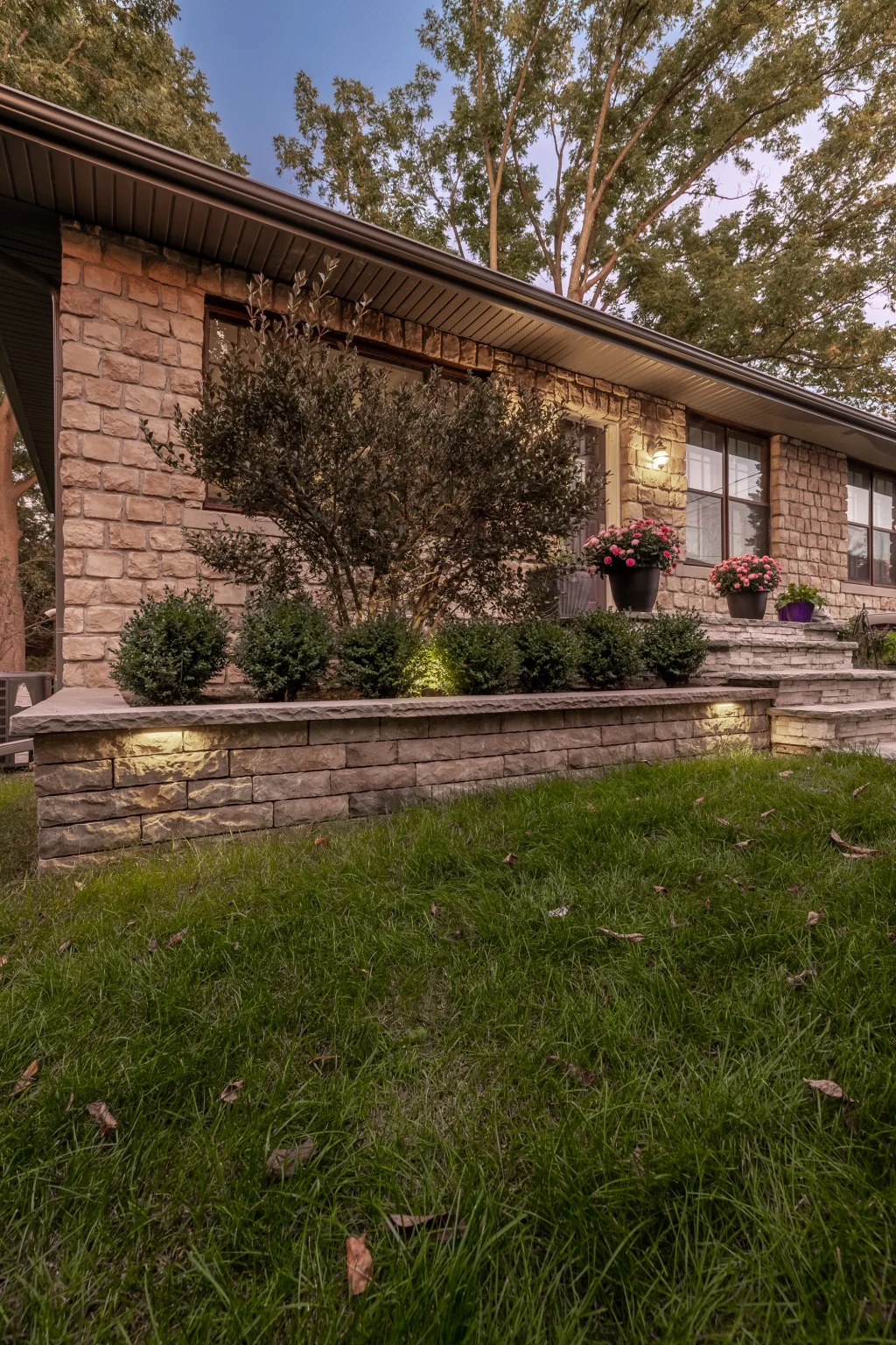Dusk portrait of the front lawn and raised landscape wall beside the stone home in Hamilton.