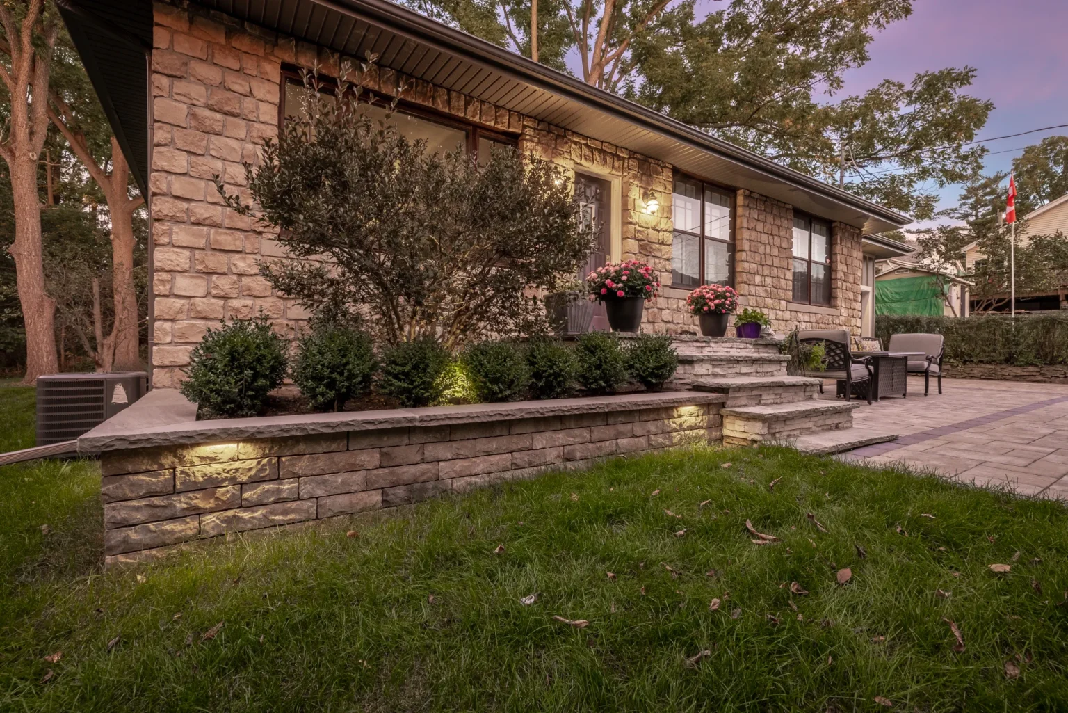 Closer dusk view of the raised front planting wall and paved entrance area in Hamilton.