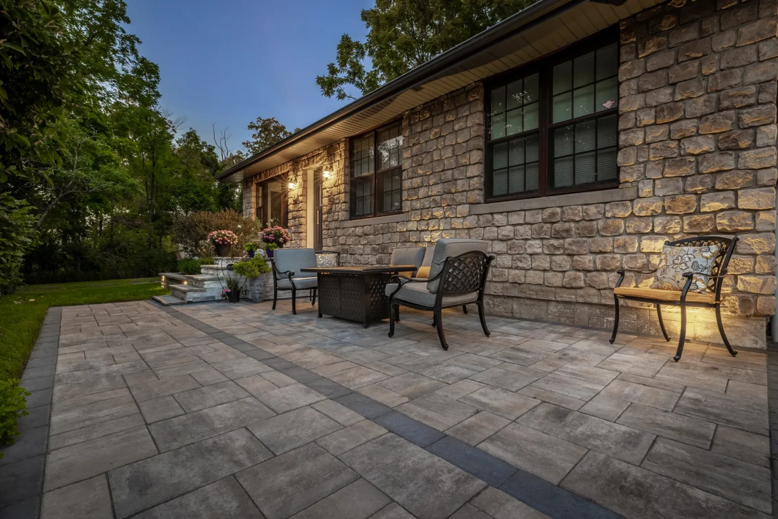 Wide front seating patio with interlock paving beside the stone house in Hamilton.