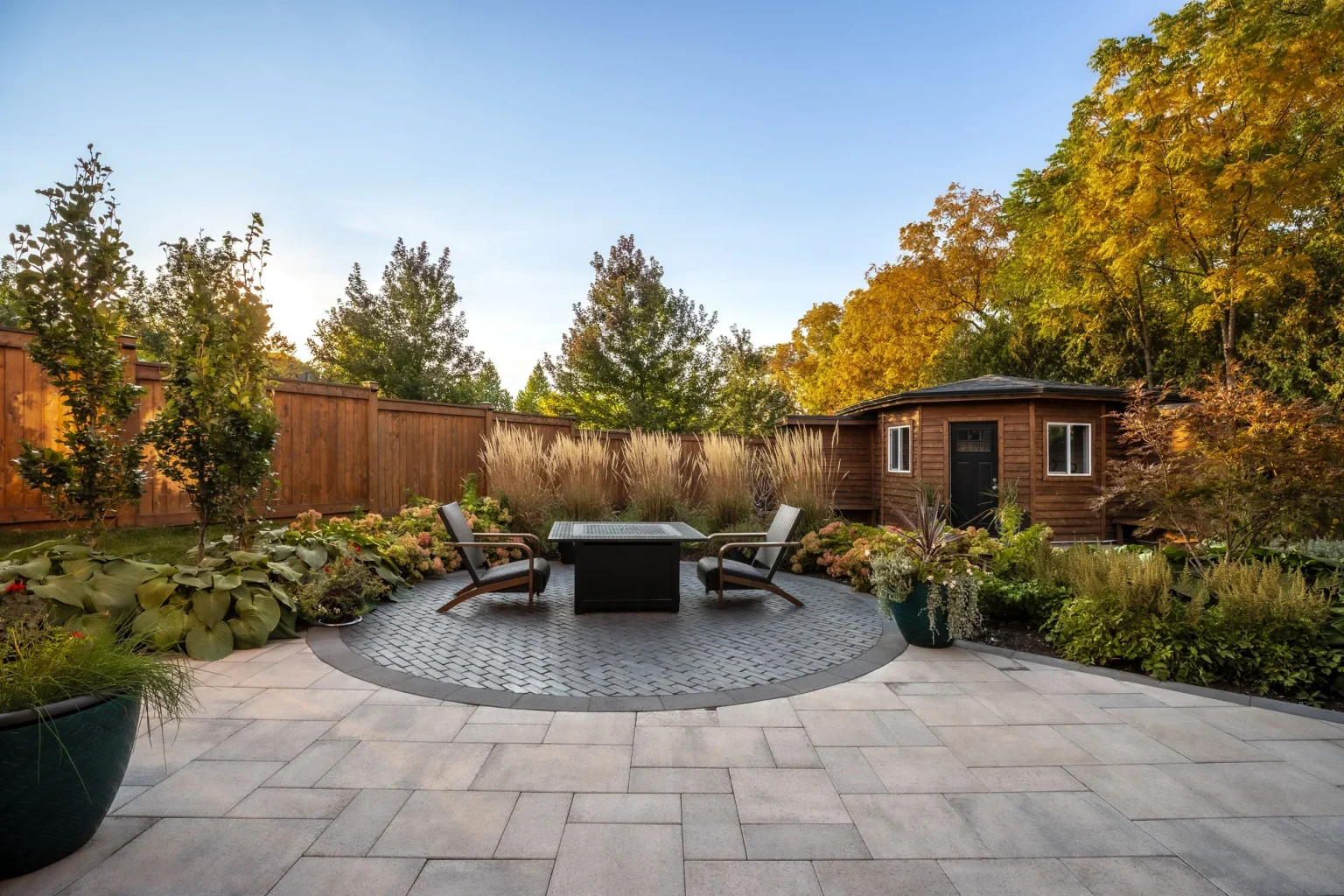 Circular paver patio with a fire table and lounge chairs, surrounded by garden beds and timber fencing in Oakville.