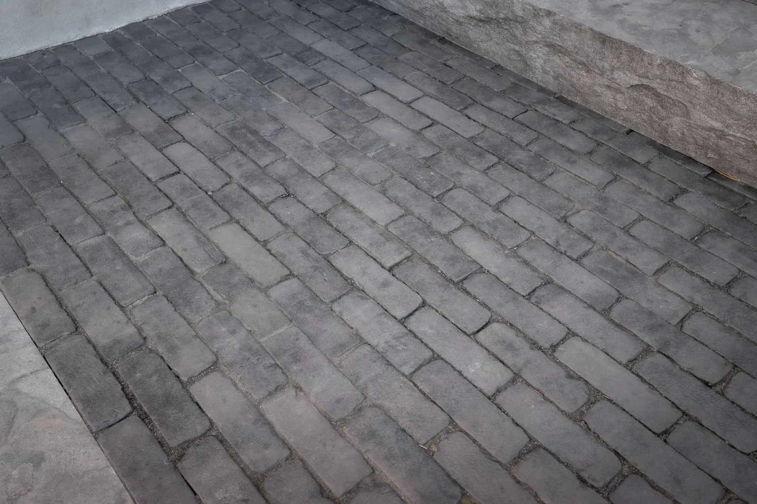 Close detail of small textured grey interlock blocks and a rough stone border on a backyard patio in Oakville.
