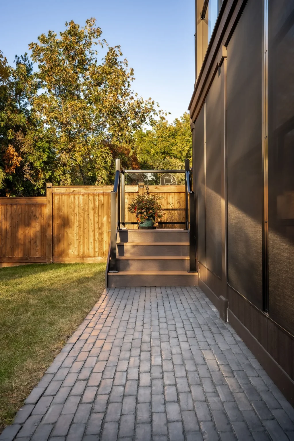 Portrait view down a narrow dark interlock walkway running between the house exterior and a wooden fence toward rear steps in Oakville.
