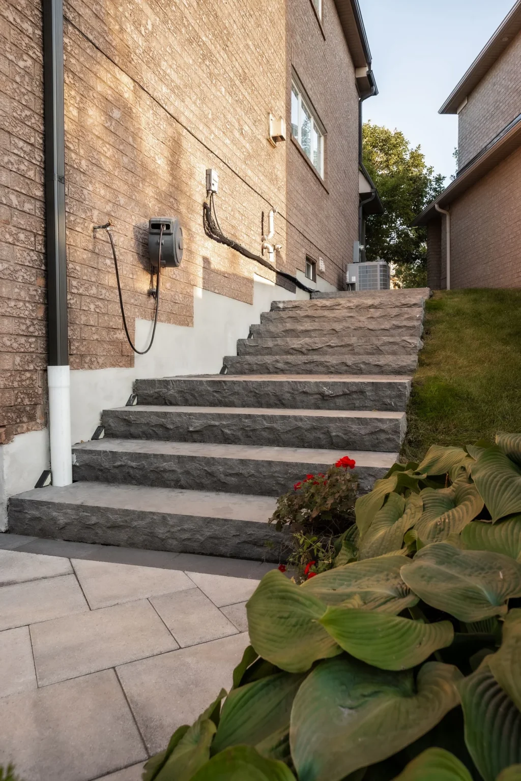 Portrait photo looking up a stepped grey stone pathway between brick house walls, with garden leaves in the foreground in Oakville.