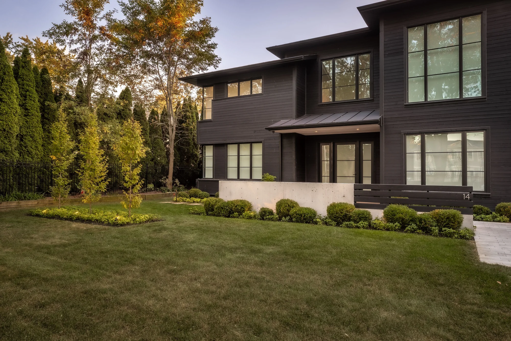A modern black home in Oakville with a broad lawn, shaped shrubs, mature trees and formal front-entry planting.